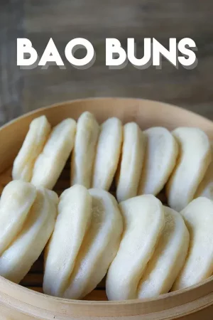 A wooden bowl containing creamy white steamed buns folded in round halves.