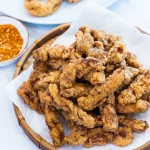 Breaded deep fried pork pieces are a golden brown color, sitting on a white plate.